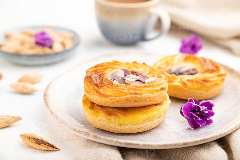 Small cheesecakes with jam and almonds with cup of coffee on a white concrete background and linen textile. Side view, close up, selective focus