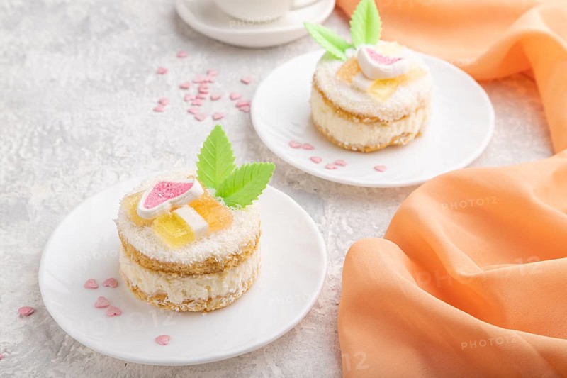 Decorated cake with milk and coconut cream with cup of coffee on a gray concrete background and orange textile. Side view, close up