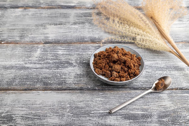 Plate with unrefined brown cane sugar on gray wooden background. side view, copy space