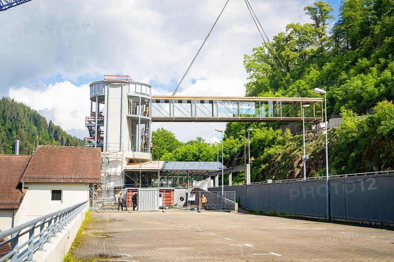 A lifted bridge over a building complex, held by a crane, in sunny weather with blue sky and white clouds, watched by people, bridge lifting Hermann Hesse railway, Calw, Germany, Europe