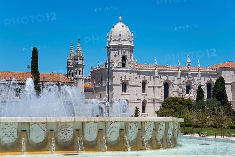 Eine gotische Kathedrale mit imposanten Türmen und einem verzierten Brunnen davor, unter einem klaren blauen Himmel, Hieronymus Kloster, Mosteiro dos Jerónimos, Hieronymitenkloster, Weltkulturerbe, Klosterkirche Santa Maria, Belém, Belem, Bethlehem, Lissabon, Lisboa, Portugal, Europe