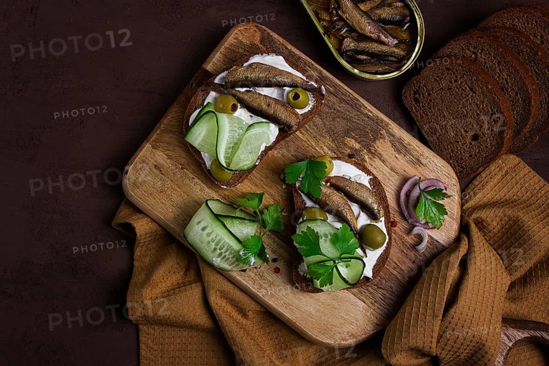 Sandwiches, black bread with sprats, cream cheese, cucumbers, on a cutting board, top view, close-up, no people