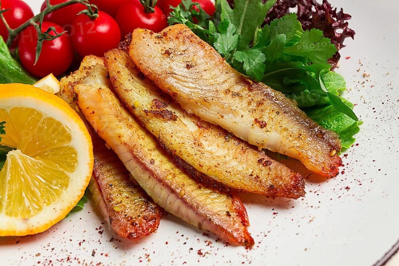 Fried Tilapia fish fillet, in spices, with cherry and salad, on a white plate, homemade, no people
