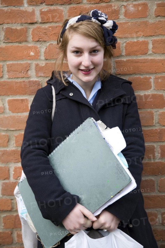 Model released portrait of teenage school girl with her art folders standing against brick wall, England, UK