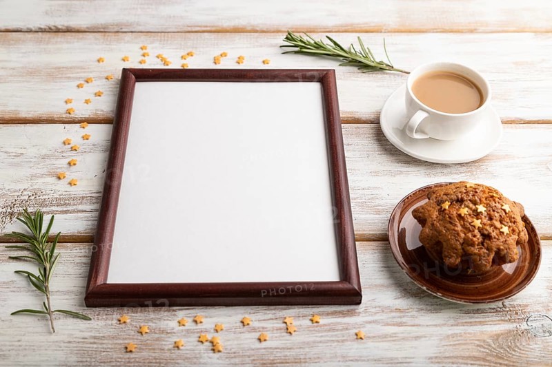Brown wooden frame mockup with cup of coffee and cake on white wooden background. Blank, side view, still life