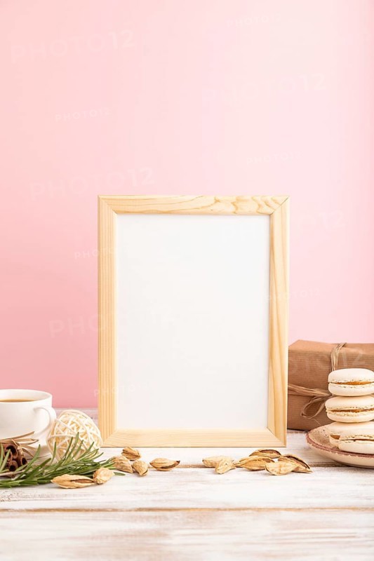 White wooden frame mockup with cup of coffee, almonds and macaroons on pink pastel background. Blank, side view, still life
