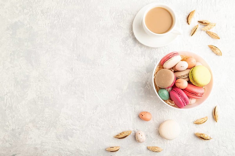 Multicolored macaroons and chocolate eggs in ceramic bowl, cup of coffee on gray concrete background. top view, copy space, still life. Breakfast, morning, concept