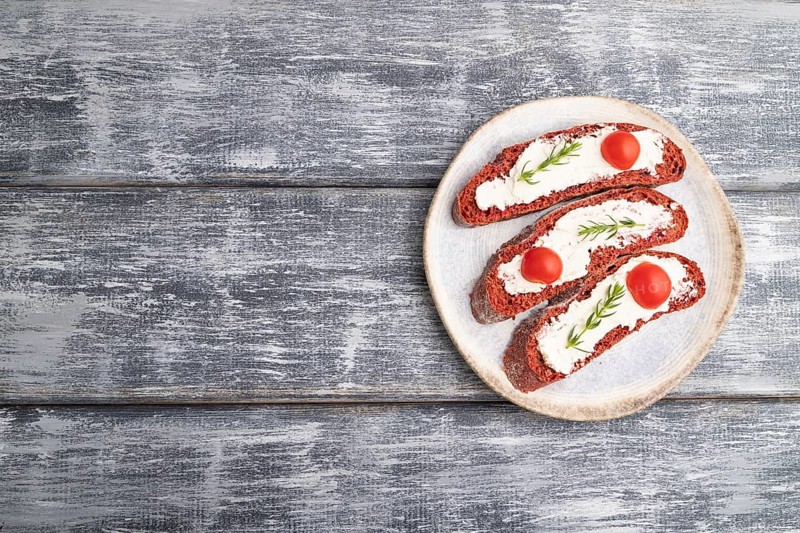 Red beet bread sandwiches with cream cheese and tomatoes on gray wooden background. top view, flat lay, copy space