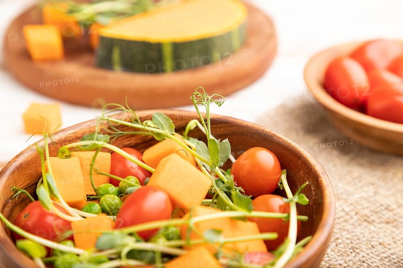 Vegetarian vegetable salad of tomatoes, pumpkin, microgreen pea sprouts on white wooden background and linen textile. Side view, close up, selective focus