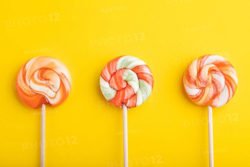 Three lollipop candies on yellow pastel background. copy space, top view, flat lay