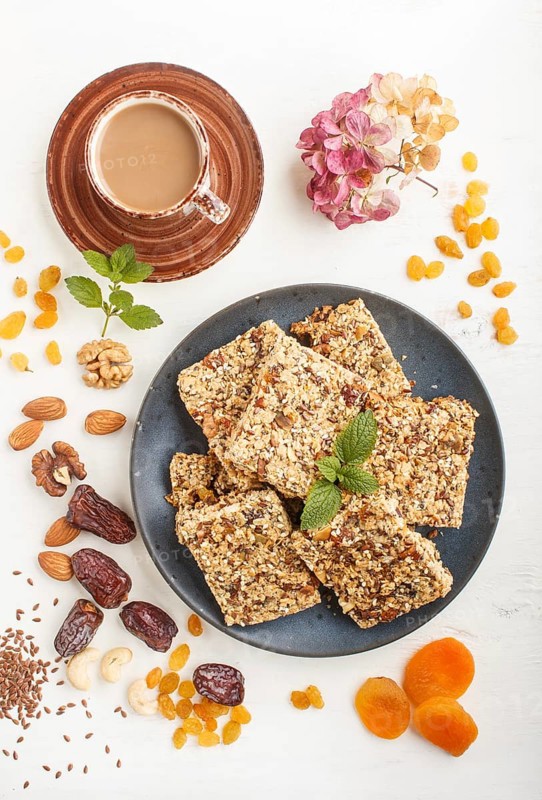 Homemade granola from oat flakes, dates, dried apricots, raisins, nuts in blue ceramic plate with a cup of coffee on a white wooden background. Top view, flat lay, close up