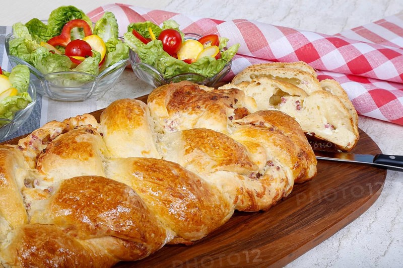 Swabian cuisine, hearty yeast plait with smoked meat, salty wreath bread, yeast yeast dough pastry, arranged on wooden board, baked, grandmother's kitchen, regional, home cooking, typical Swabian reinterpreted, traditional cuisine reinterpreted, salad in the back, small bowl, food photography, studio, Germany, Europe
