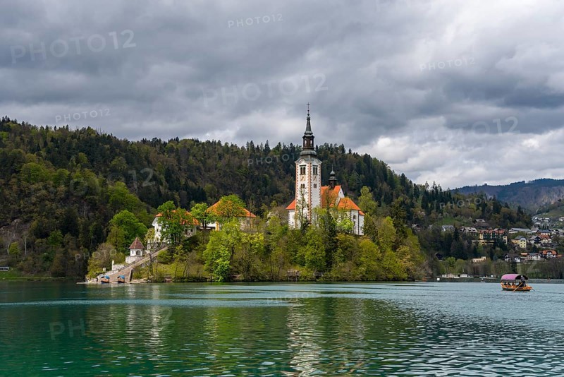 Church on an island in the lake under a cloudy sky, with a boat in the water, Bled Island with St Mary's Church, Lake Bled, Lake Veldes, Blejsko jezero, Bled, Veldes, Feldes, Upper Carniola region, Gorenjska, Slovenia, Balkans, Europe