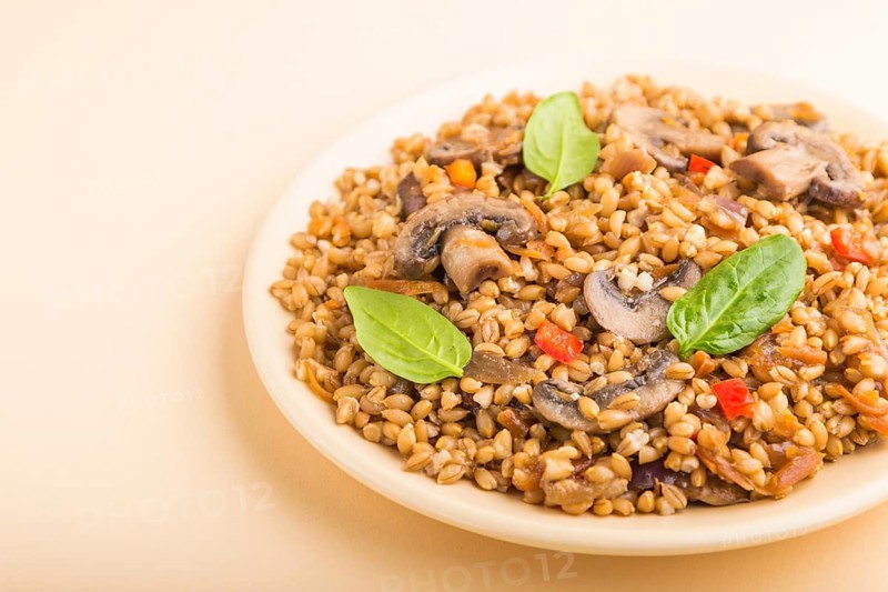 Spelt (dinkel wheat) porridge with vegetables and mushrooms on ceramic plate on orange background. Side view, close up. Russian traditional cuisine