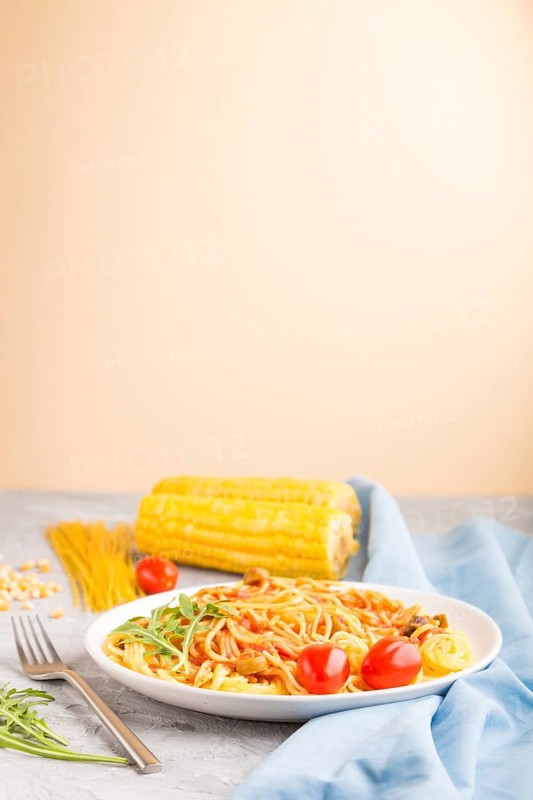 Corn noodles with tomato sauce and arugula on a gray and orange background and blue textile. Side view, copy space, selective focus