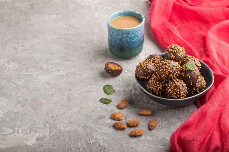 Chocolate caramel ball candies with almonds and a cup of coffee on a gray concrete background and red textile. Side view, copy space