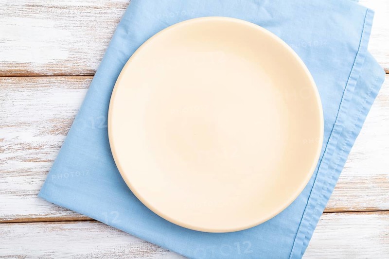 Empty ceramic plate on white wooden background and blue linen textile. Top view, close up, flat lay