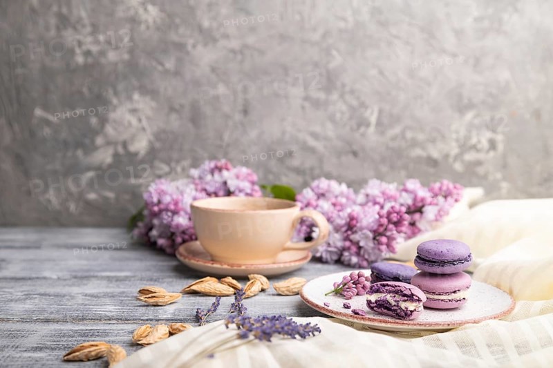Purple macarons or macaroons cakes with cup of coffee on a gray wooden background and white linen textile. Side view, copy space