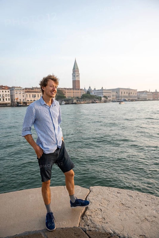Young man in striped shirt and shorts on the banks of the Grand Canal, behind Campanile, Venice, Veneto, Italy, Europe