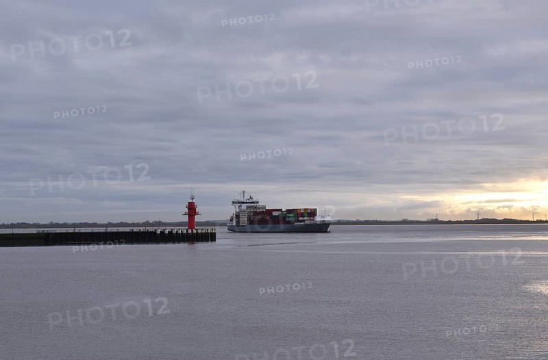 Container ship Beate sails on the Elbe at sunset and turns into the Brunsbüttel lock to the Kiel Canal, NOK. Schleswig-Holstein, Germany, Europe