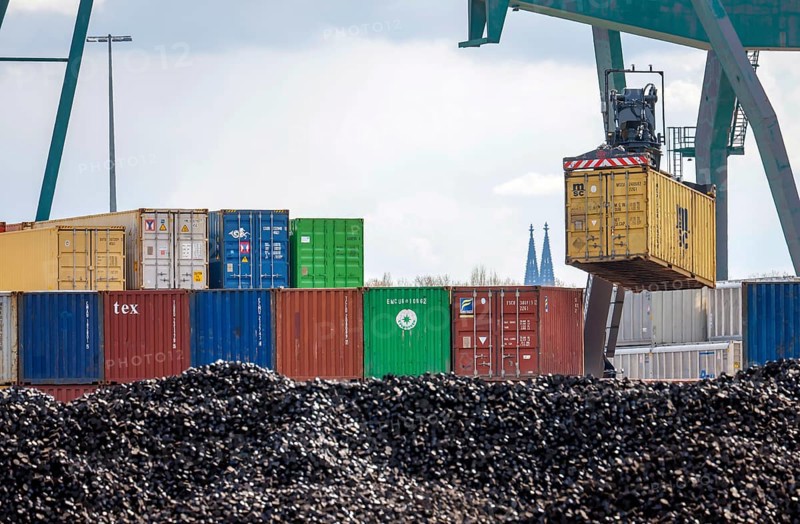 Cologne, North Rhine-Westphalia, Germany - Port of Cologne Niehl, container warehouse at the container terminal, harbour crane lifts containers, Cologne Cathedral towers in the back, bulk goods in front