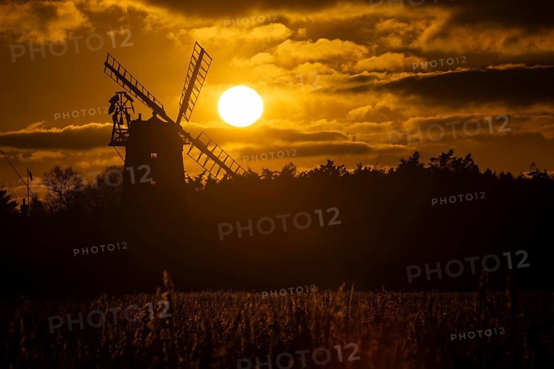 Windmill silhouette at sunset with a red sky and clouds behind and reedbed in the foreground, Cley-next-to-the-sea, Norfolk, England, United Kingdom, Europe