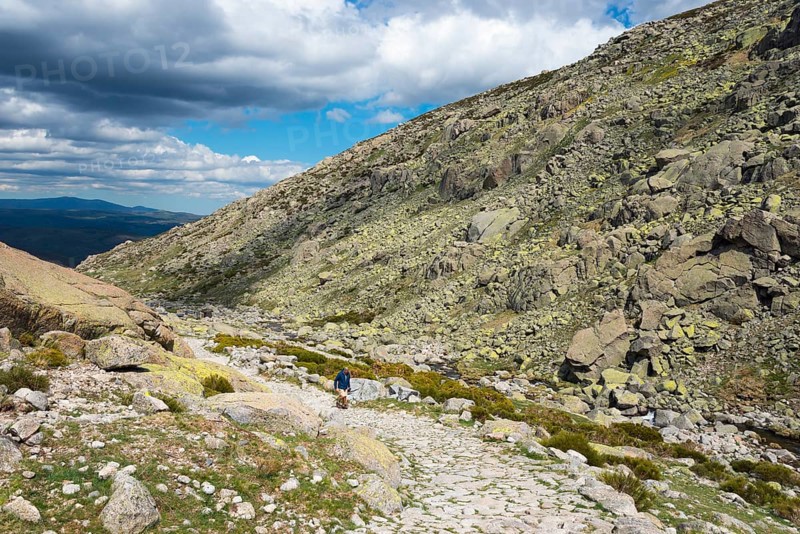 A hiking person on a stony path through a rocky mountain landscape under a cloudy sky, Hiking area, Reserva national de Gredos, Garganta de Prado Puerte, Prado Puerte Gorge, Sierra de Gredos, Ávila, Avila, Madrid, Spain, Europe