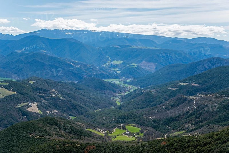 Weitreichende Berglandschaft mit einem grünen Tal, bewaldeten Hängen und einem blauen Himmel mit Wolken, Blick vom Aussichtspunkt des Creu de Guils, in der Nähe der N-260, Lleida, Katalonien