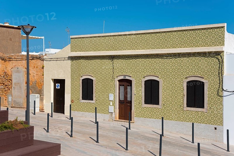 Rustic house with green façade, shutters and street lamp. Sunny street in the foreground, house with azulejos, Fuseta, Fuzeta, Faro, Algarve, Portugal, Europe