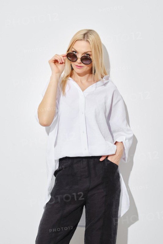 Blonde woman in white shirt and black trousers looking to the side with her sunglasses lowered