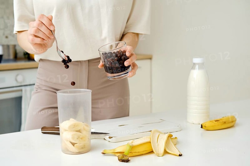 Unrecognizable woman puts blackcurrants in a blender to mix them with a chopped banana