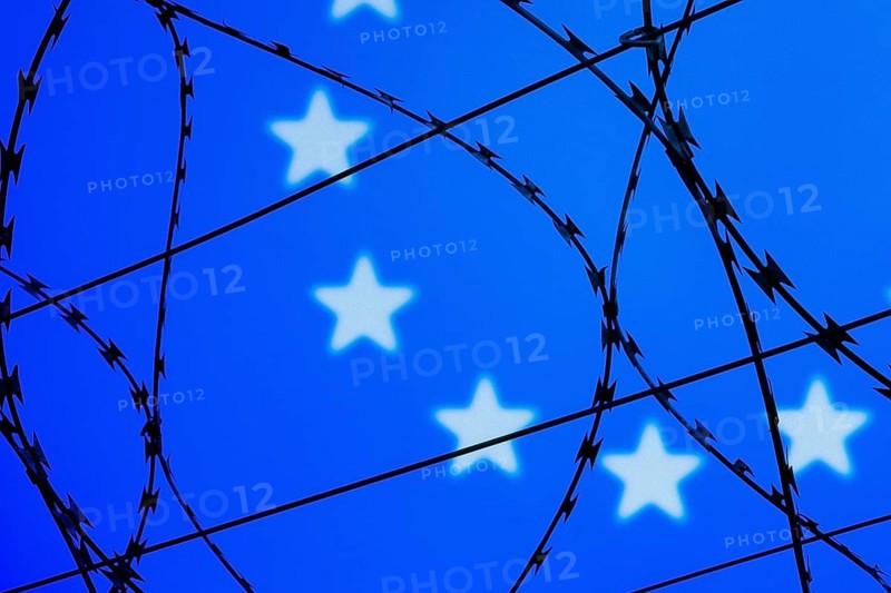 Symbolic image, migration, defence against refugees wanting to enter the EU, barbed wire overarches the stars of the EU flag against a blue sky, border, border fence