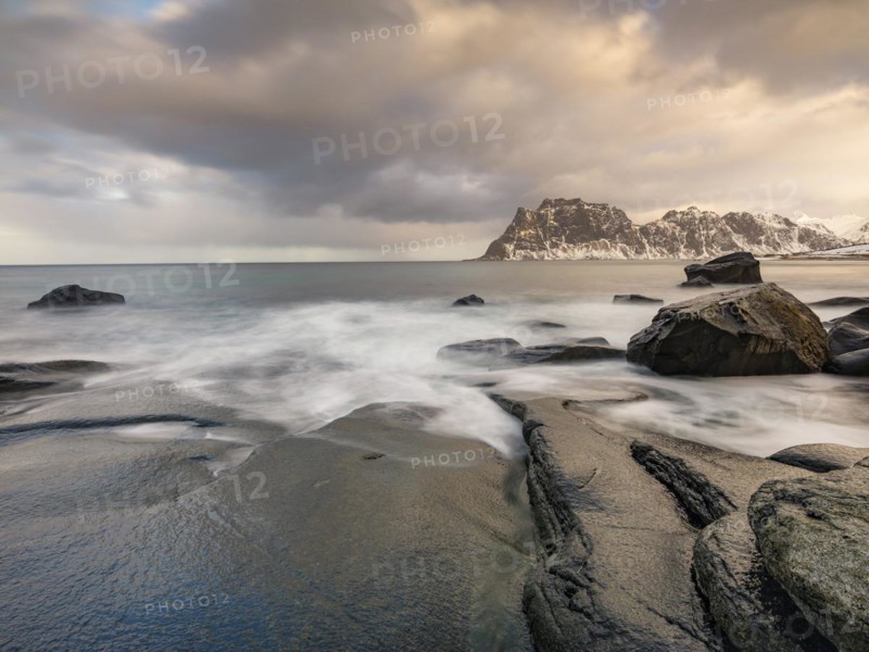 Smoothly polished rocks on Utakleiv beach in a dramatic cloudy atmosphere, snow-capped mountains in the background, Vestvagoy Island, Lofoten, Norway, Europe