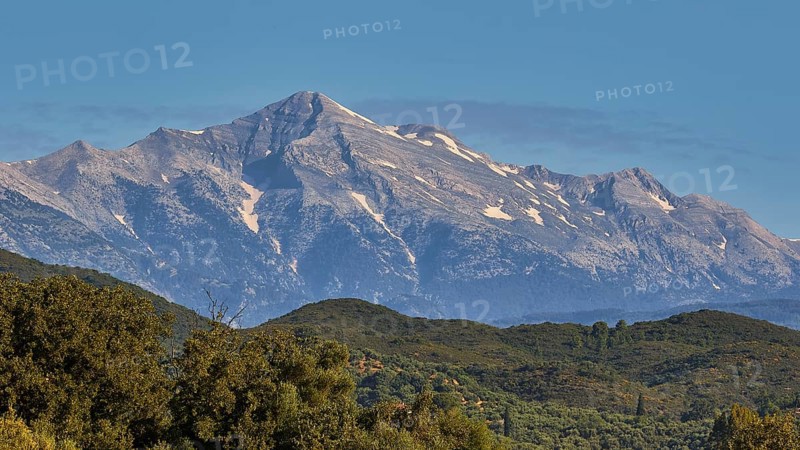 A majestic, snow-capped mountain peak rises above green forests, Taygetos Mountains, Mani Peninsula, Peloponnese, Greece, Europe