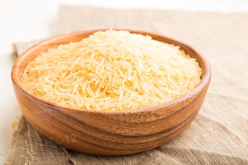Wooden bowl with raw golden rice and wooden spoon on a white wooden background and linen textile. Side view, close up, selective focus