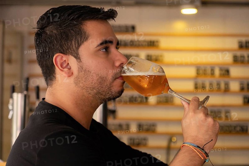 A young man enjoys a glass of beer in a cozy pub or restaurant. The warm and cozy atmosphere enhances the moment, capturing the essence of relaxation and social enjoyment