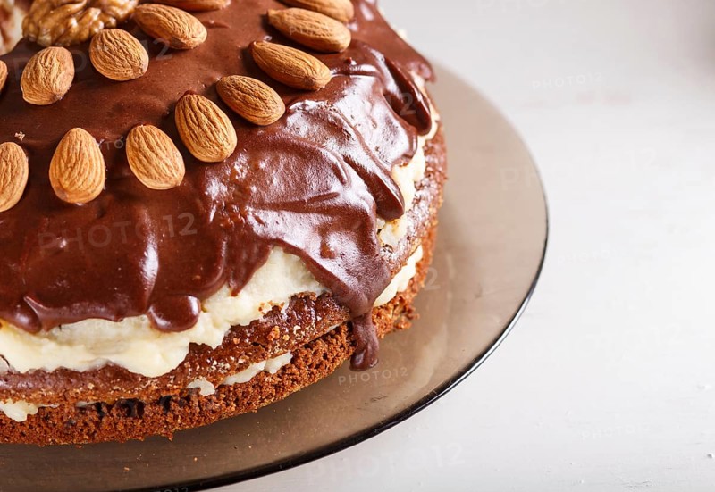 Homemade chocolate cake with milk cream, caramel and almonds on white wooden background. close up