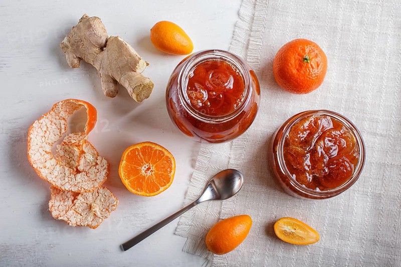 Tangerine and kumquat jam in a glass jar with fresh fruits on white wooden background. Homemade, top view