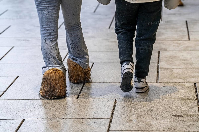2 woman walking in the rain, one woman wears boots with long fur, wet, dirty, water splashes on her trousers