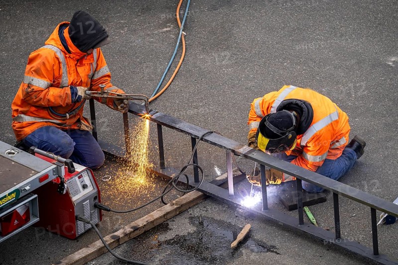Locksmith at work, cutting and welding, on a workpiece in an industrial plant, a metal ladder is split with a welding torch, a welder fixes a ladder rung with a welding machine