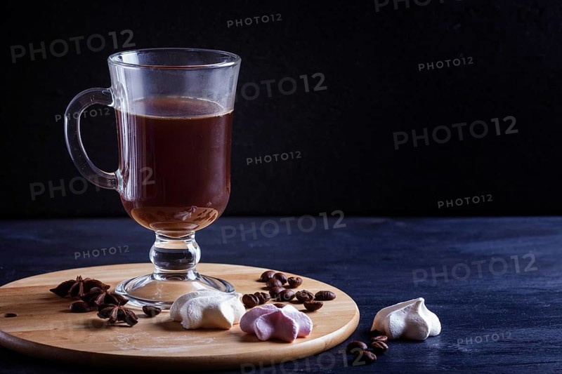 Glass cup of coffee with meringues on a wooden board on a black background. close up, copy space