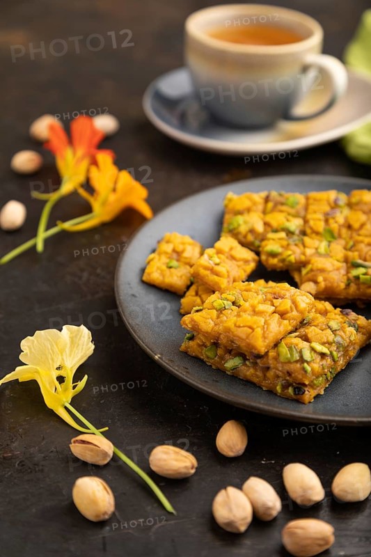 Traditional iranian dessert sohan with cup of green tea on a black concrete background and green textile. side view, close up, selective focus