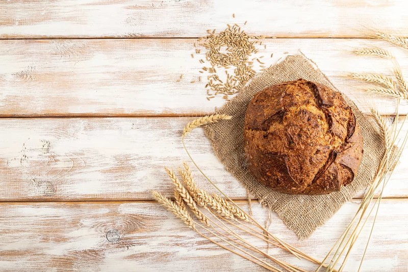 Fresh homemade golden grain bread with ears of wheat and rye on white wooden background and linen textile. top view, flat lay, copy space
