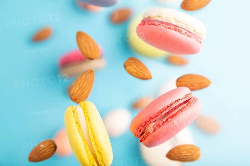 Multicolored flying macaroons and almonds eggs frozen in the air on blurred blue background. top view, flat lay, close up. Breakfast, morning, concept