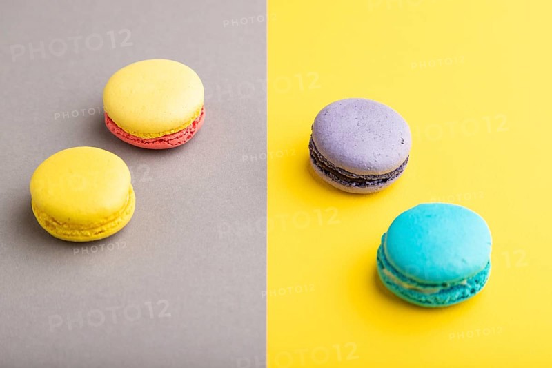 Yellow, purple and blue macaroons on trendy gray and yellow background. side view, copy space, close up, still life. Minimalism, morning, contrast concept