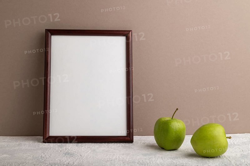 Brown wooden frame mockup with green apple on beige paper background. Blank, vertical orientation, still life, copy space
