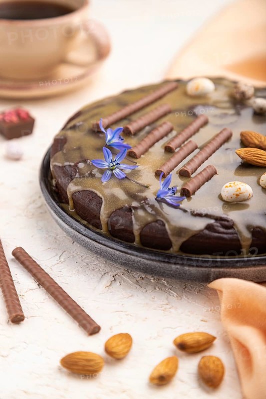Homemade chocolate brownie cake with caramel cream and almonds with cup of coffee on a white concrete background and orange textile. Side view, close up, selective focus