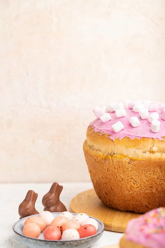 Homemade glazed and decorated easter pies with chocolate eggs and rabbits on a white concrete background and yellow textile. Side view, copy space, selective focus
