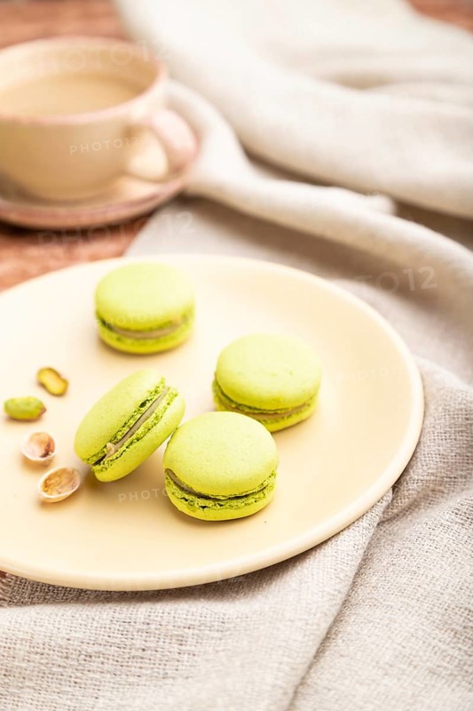 Green macarons or macaroons cakes with cup of coffee on a brown concrete background and linen textile. Side view, close up, selective focus
