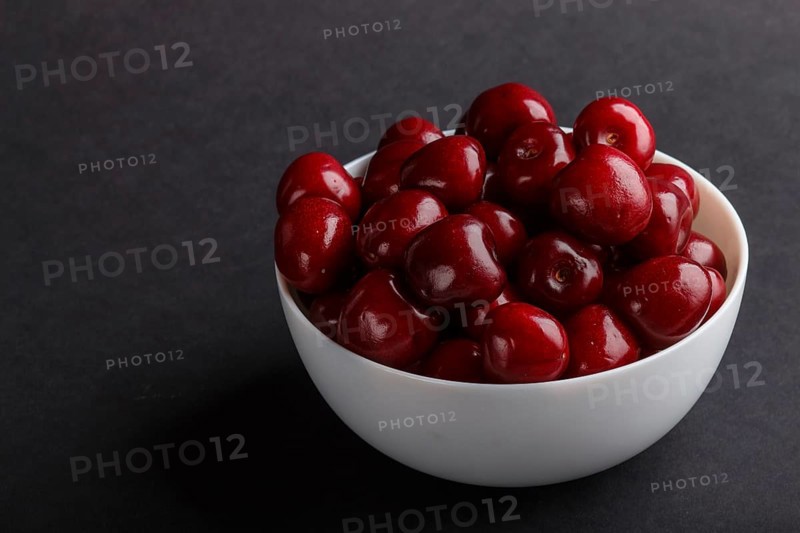 Fresh red sweet cherry in white bowl on black background. side view, close up